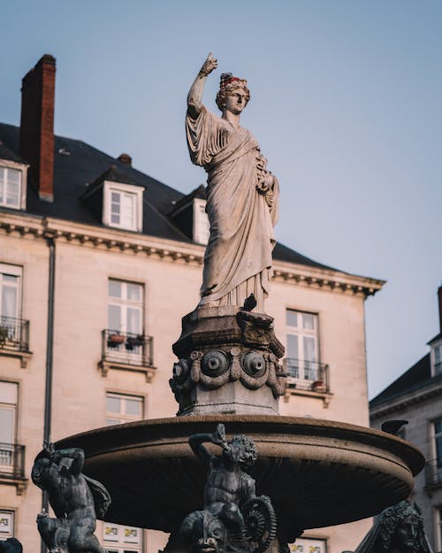 Old stone statue near building facade under blue sky