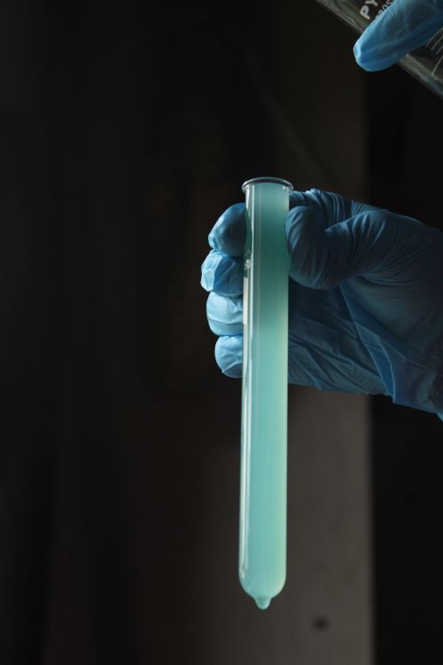 Free Close-up of a gloved hand holding a test tube with blue liquid in a lab setting. Stock Photo