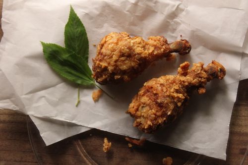 Free Two crispy fried chicken drumsticks with green leaves on parchment paper. Stock Photo