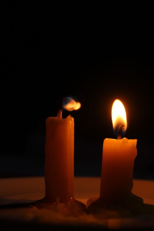 Free Two candles, one lit and one extinguished, glow warmly against a dark background. Stock Photo