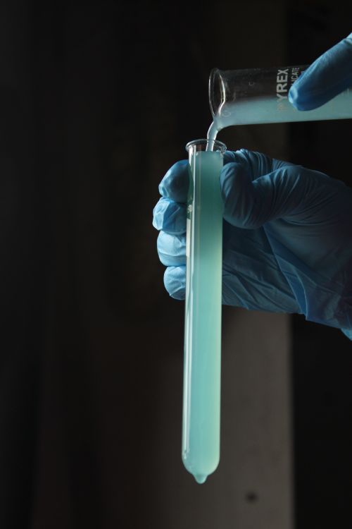 Free Close-up of gloved hands pouring liquid into a test tube in a dark lab setting. Stock Photo