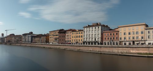 Free A serene view of colorful riverfront buildings in Pisa, Italy alongside a calm river. Stock Photo