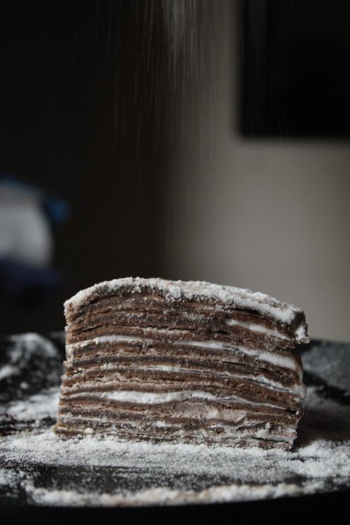 Free A close-up of a chocolate crepe cake being sprinkled with powdered sugar. Stock Photo