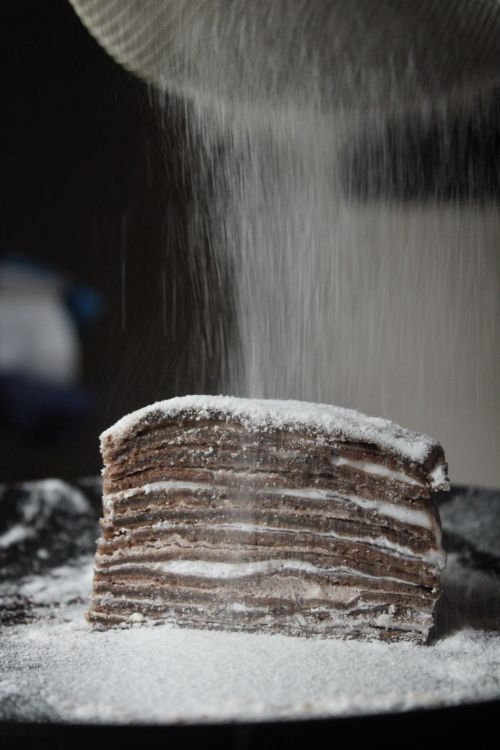 Free Close-up of layered chocolate crepe cake being dusted with icing sugar. Stock Photo