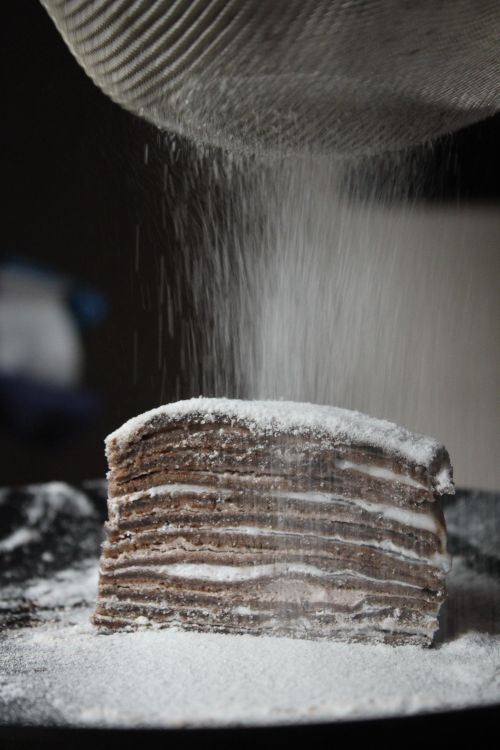 Free Close-up of a layered chocolate cake being dusted with powdered sugar, creating a cozy homemade feel. Stock Photo