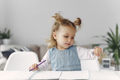 Free Young girl engaged in playful and creative learning with a toy and notebook indoors. Stock Photo