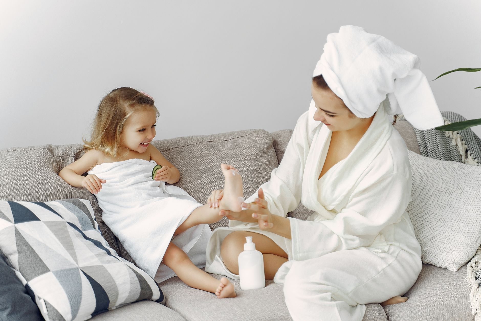 A mother and daughter enjoy bonding time on the sofa in cozy bathrobes, creating a warm family moment.