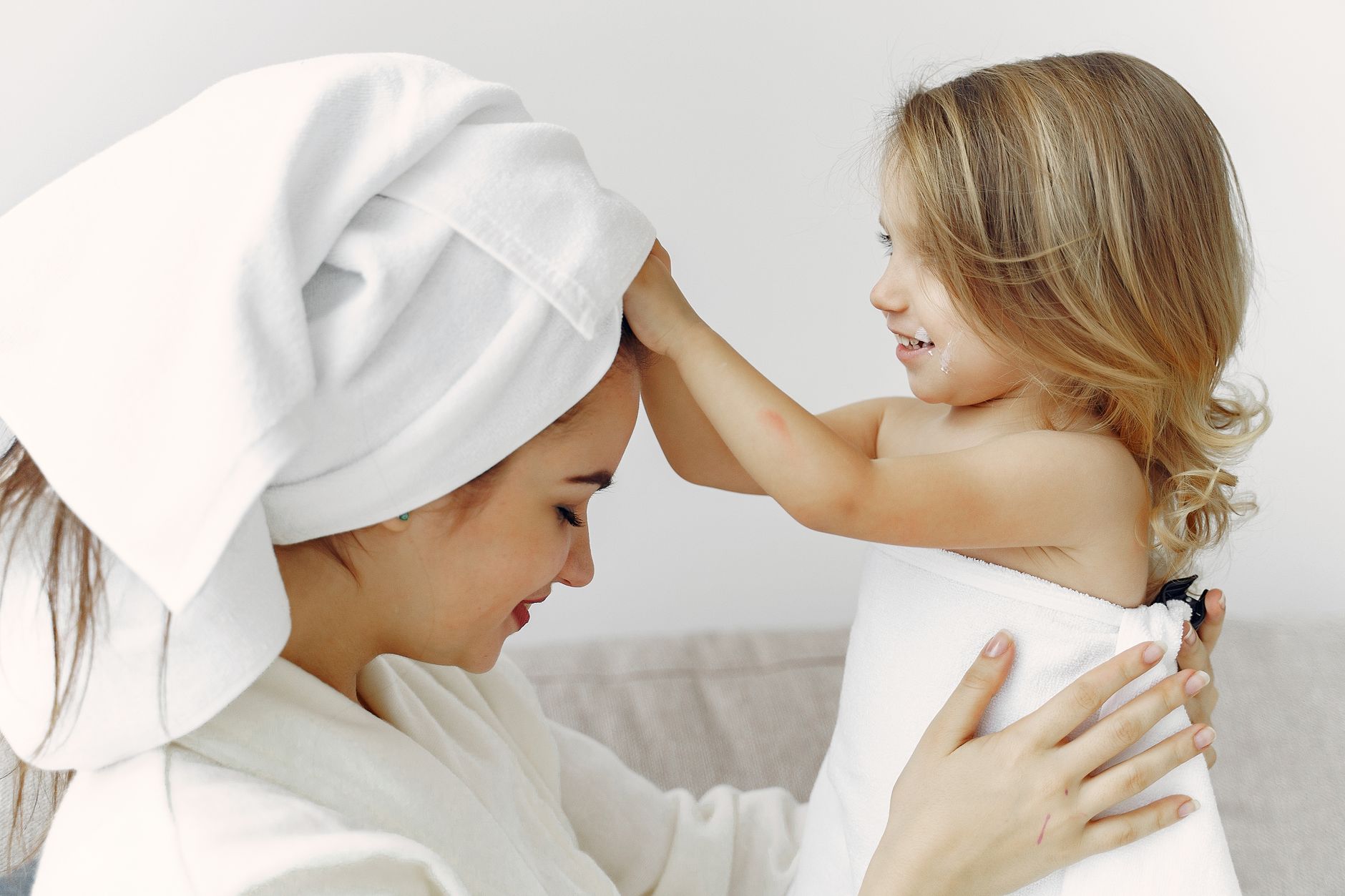 Cheerful mother and daughter bonding during bath time wrapped in cozy towels indoors.