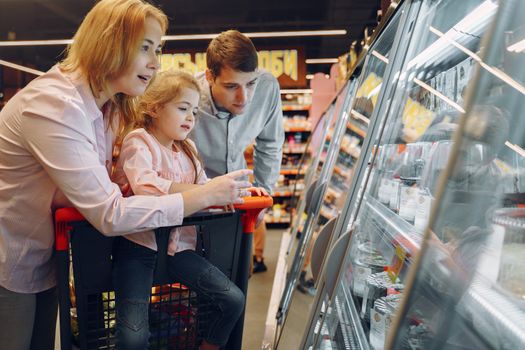 A happy family shopping together in a supermarket, exploring a refrigeration aisle.