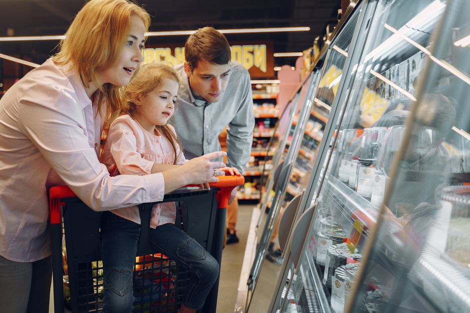 A happy family shopping together in a supermarket, exploring a refrigeration aisle.