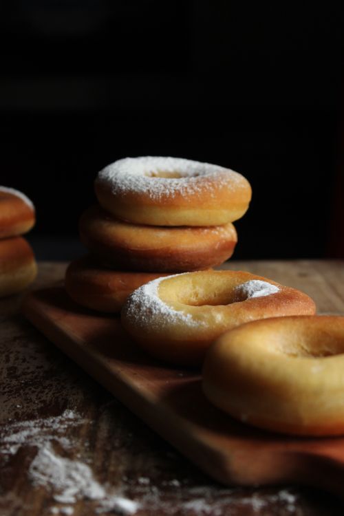 Free Freshly baked donuts with powdered sugar stacked on a wooden board. Stock Photo