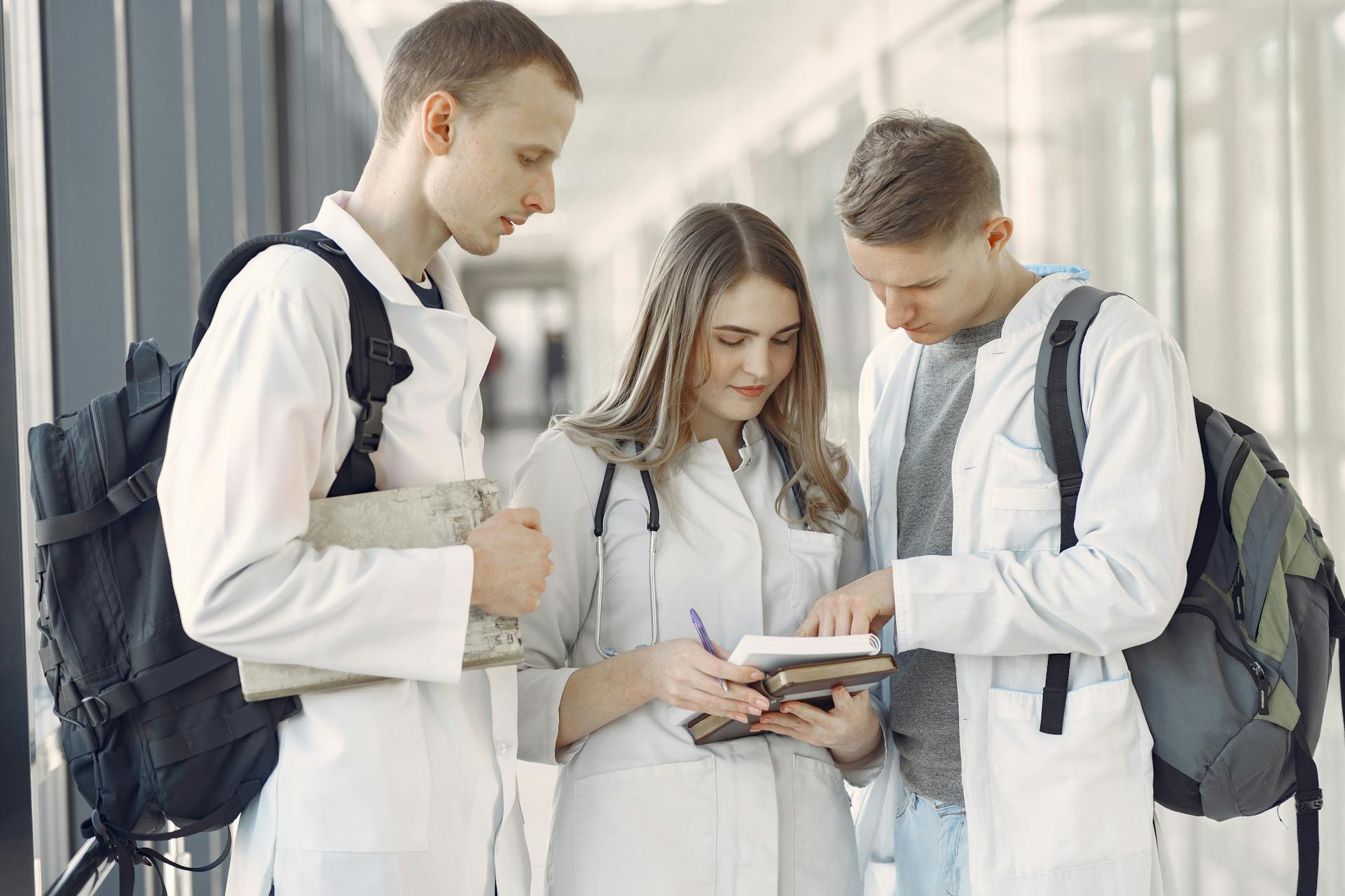 Three medical students in a hallway discussing notes, fostering teamwork and learning.