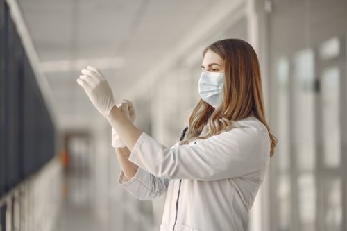Free A female doctor adjusts her gloves in a hospital hallway, emphasizing safety and professionalism. Stock Photo