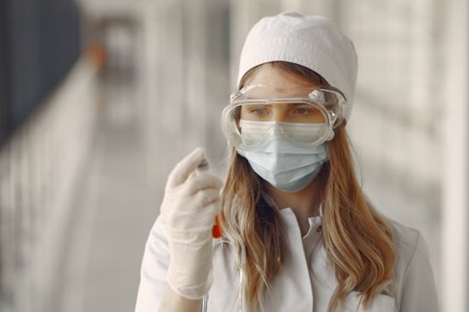 Young female scientist wearing protective gear examines a test tube in the laboratory.