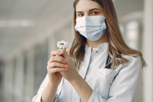 Woman in White Button Up Shirt With White Face Mask Holding White Flower