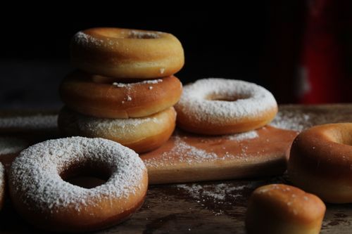 Free Stack of fresh powdered donuts displayed on a wooden board with a dark background. Stock Photo