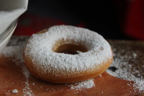 Free Close-up of a donut with powdered sugar on a rustic wooden table. Stock Photo