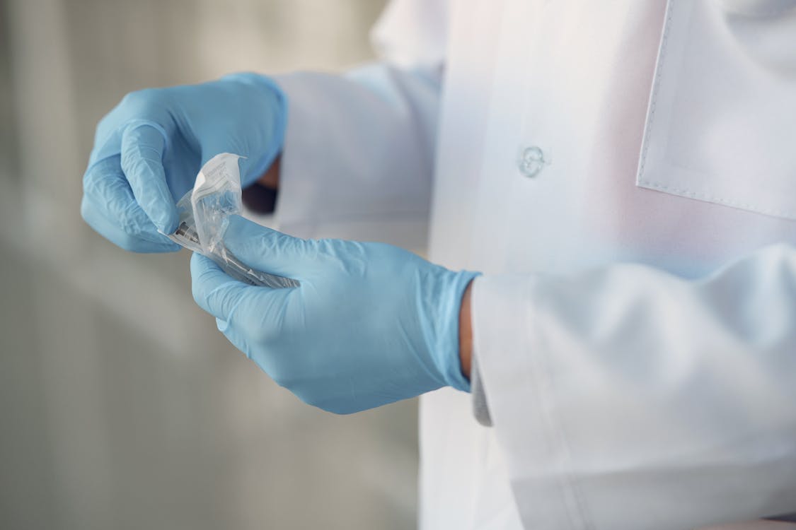 Person in Lab Gown Wearing Blue Gloves Opening Sterile Syringe