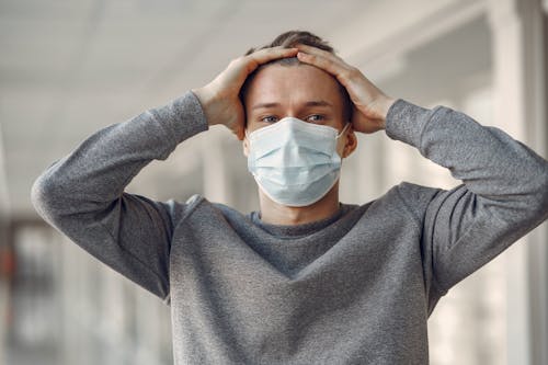 Man in Gray Sweater Covering His Face With Face Mask