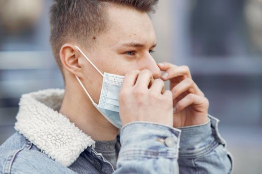A young man adjusting his face mask outdoors, highlighting personal protection and health precautions.