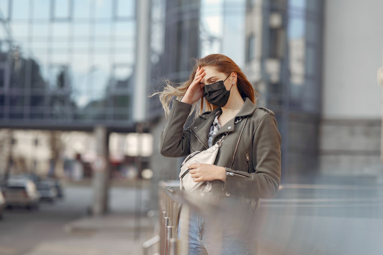 a woman wearing a face mask and stylish jacket in an urban setting cap