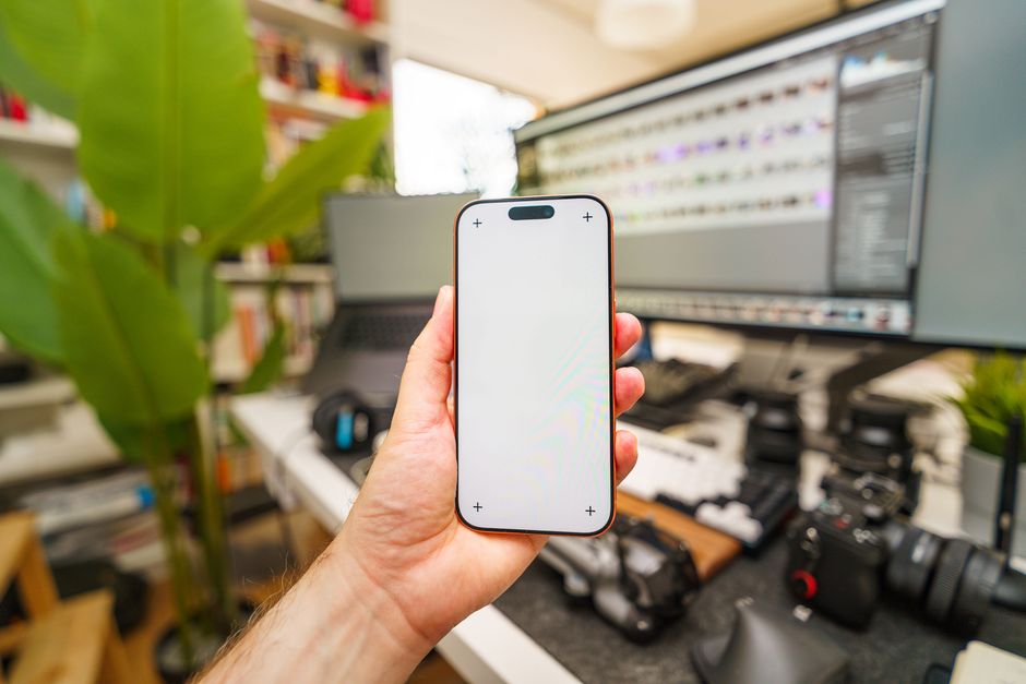 A modern workspace featuring a hand holding a smartphone with blank screen, surrounded by tech devices.