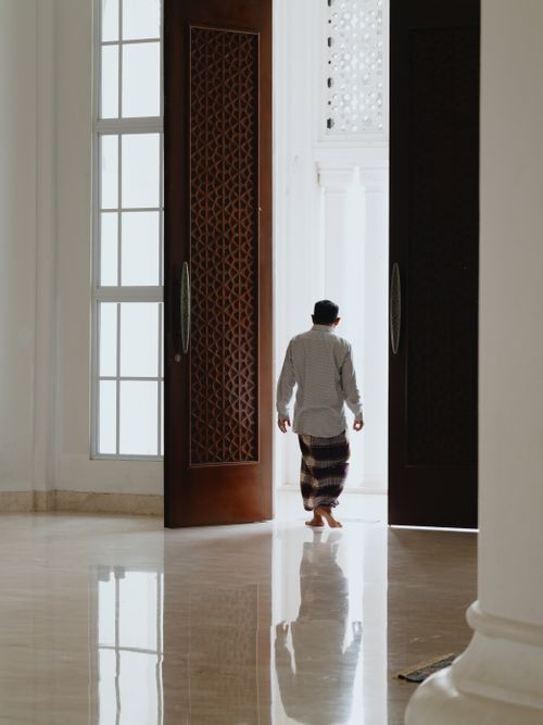 Free A man wearing traditional attire walks through the sunlit entrance of a mosque in West Java, Indonesia. Stock Photo