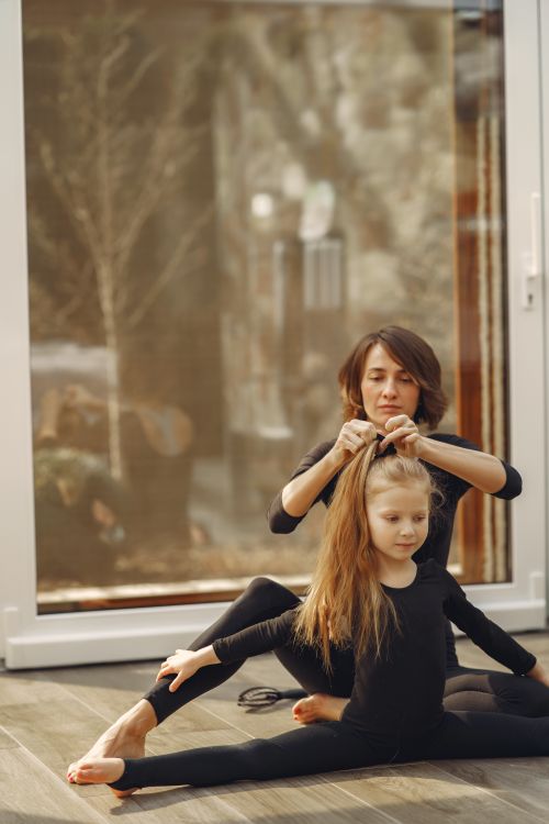 Free A mother helps her daughter stretch and fix her hair during a home workout session. Stock Photo