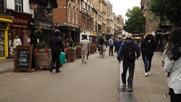 Street view of Oxford featuring pedestrians, a cyclist, and local shops in lively atmosphere.