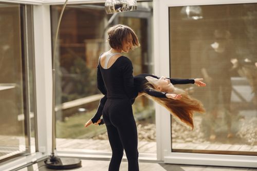 Free A happy mom and daughter bonding while dancing inside a sunlit room, sharing a precious moment. Stock Photo