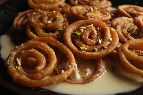 Free Close-up of sweet jalebi garnished with pistachios in syrup on a black plate. Stock Photo