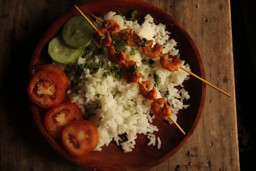 Free Appetizing dish of grilled skewers served with rice, cucumber, and tomato slices on a wooden plate. Stock Photo