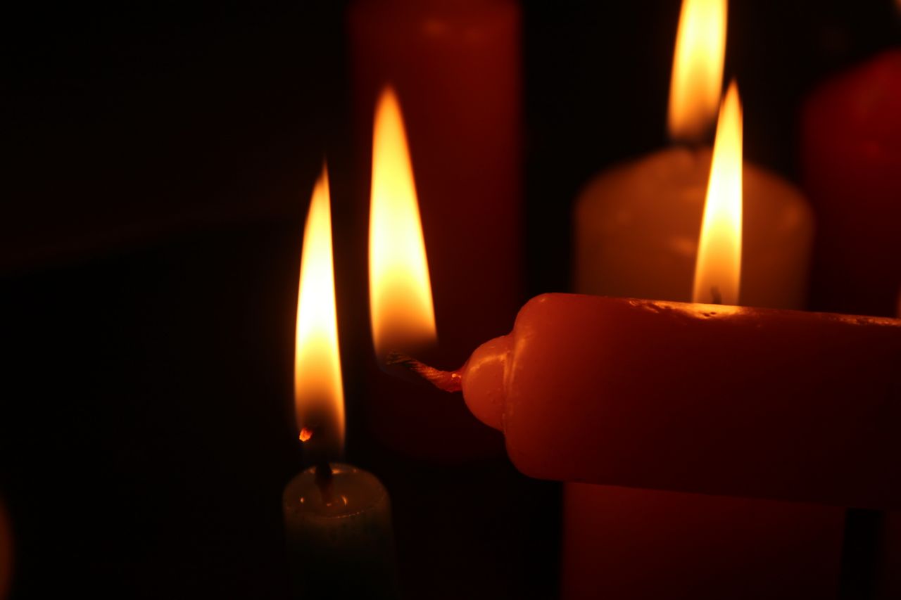 Close-up of candle flames in the dark as one candle lights another