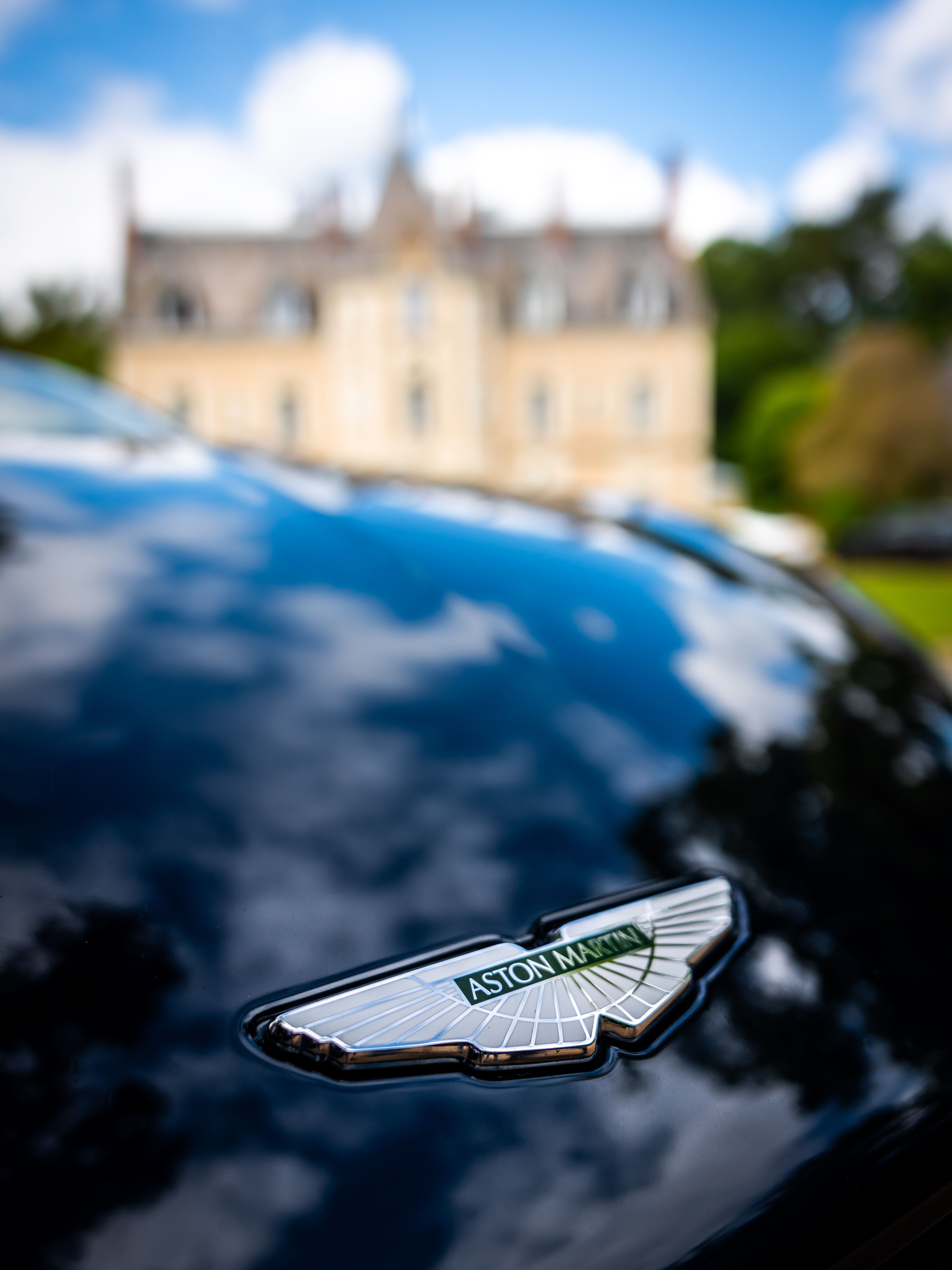 Luxury car emblem reflecting an elegant mansion under blue sky.
