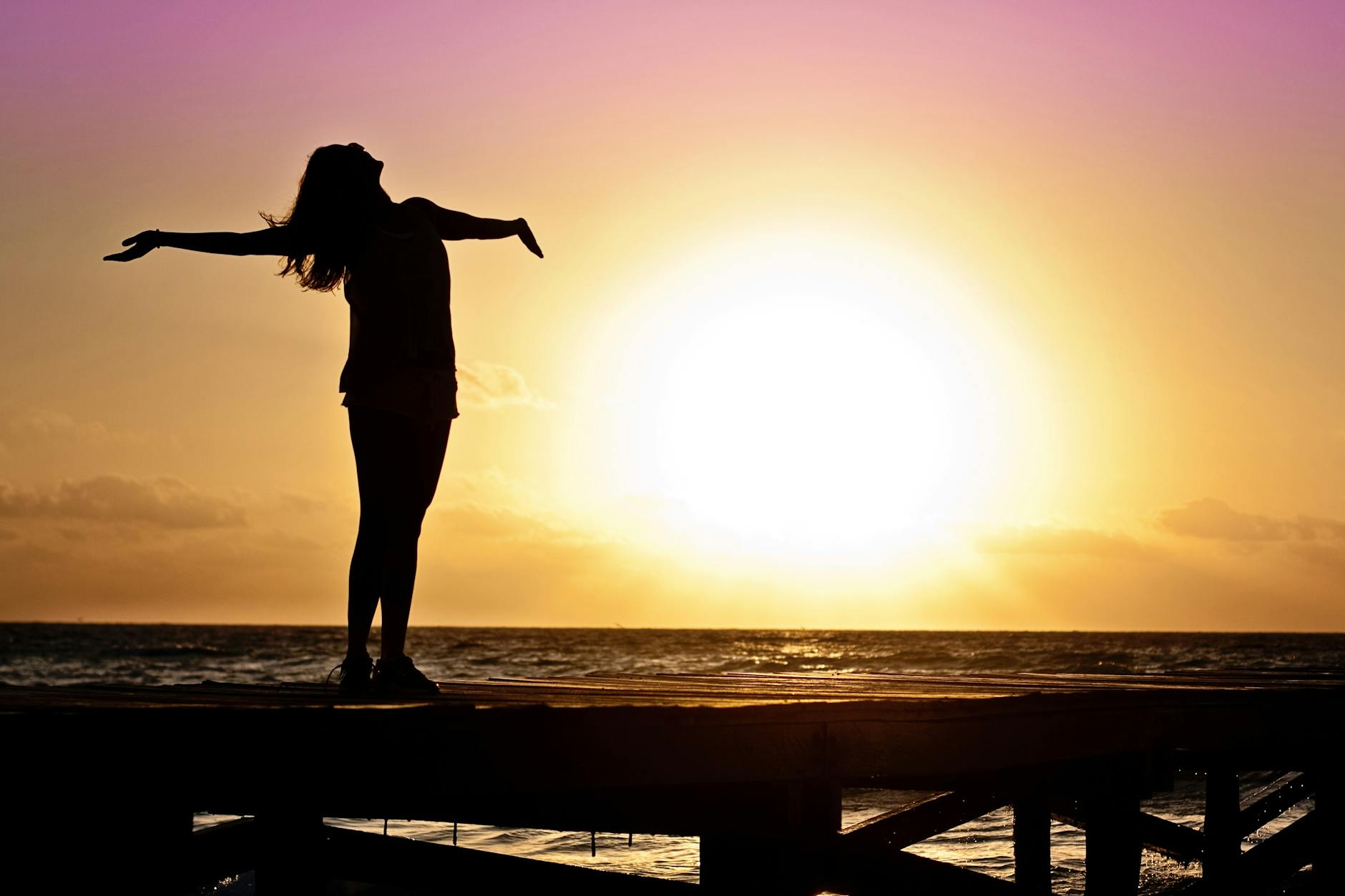 a woman stands in front of a rising sun with her arms outstretched