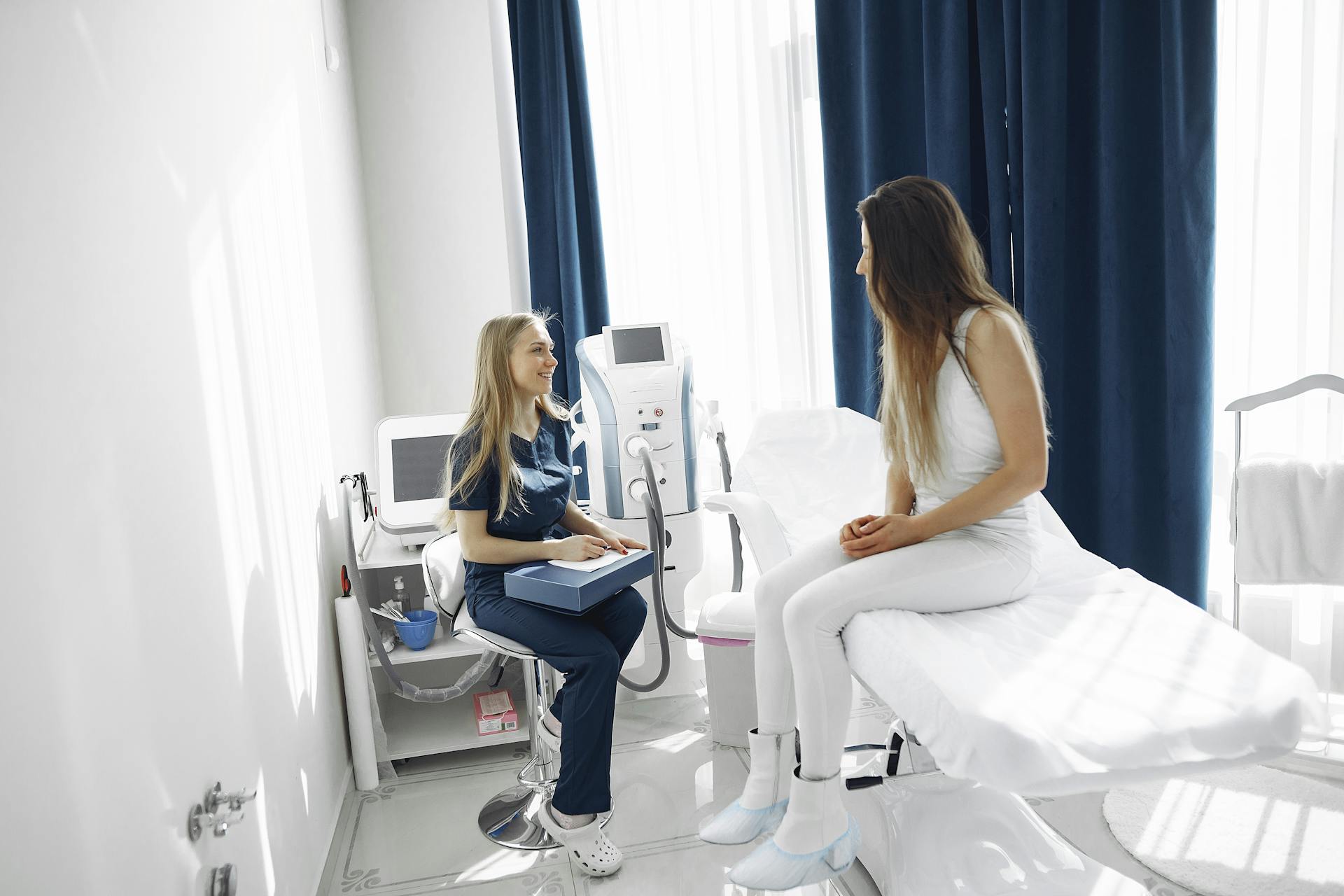 Woman in Blue Scrub Suit Helping Woman Sitting on Bed