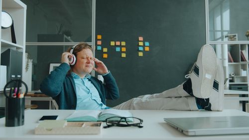 Free Man in office listening to music with headphones, sitting laid-back at desk. Stock Photo