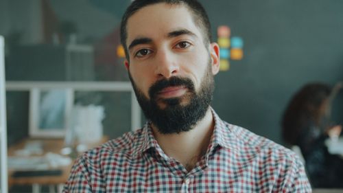 Free Close-up portrait of a bearded man in a plaid shirt, indoors in a casual office environment. Stock Photo