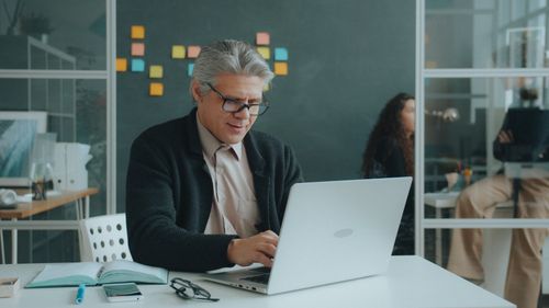 Free Professional man focusing on a laptop in a contemporary office setting with sticky notes on the wall. Stock Photo