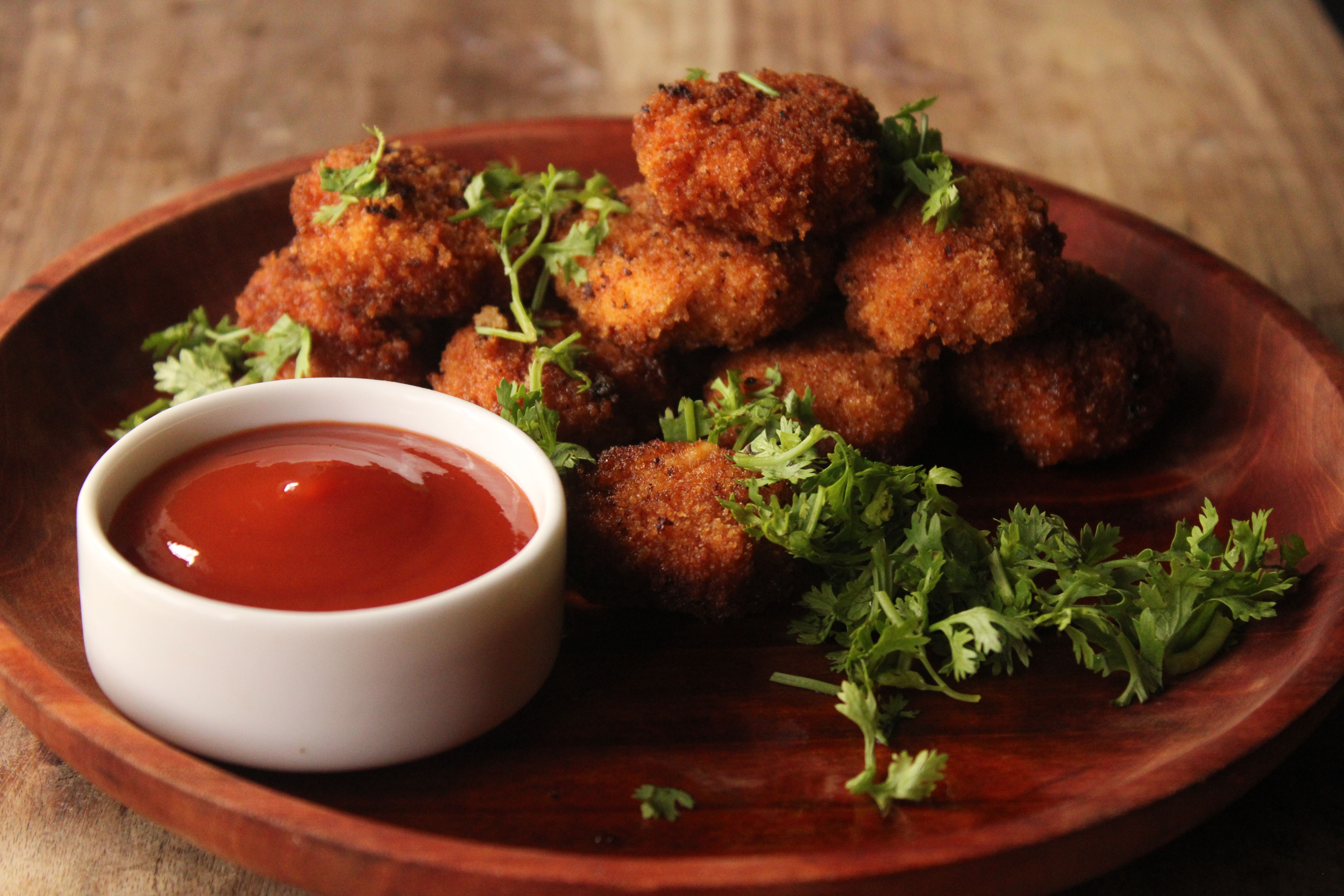 Golden crispy chicken nuggets paired with ketchup and fresh herbs on a wooden plate.