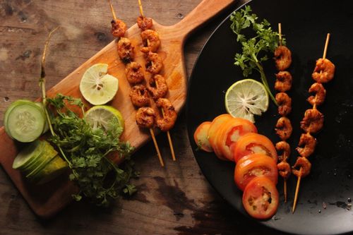 Free Delicious grilled shrimp skewers served with citrus and fresh vegetables on a wooden platter. Stock Photo