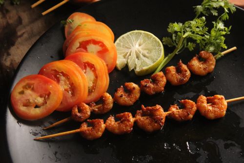Free Tasty grilled shrimp skewers with fresh tomato slices and lime on a dark plate. Stock Photo