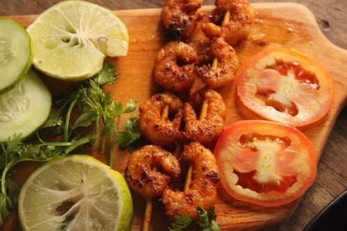Free Grilled shrimp skewers served with fresh cucumber, lime, and tomato slices on a wooden board. Stock Photo