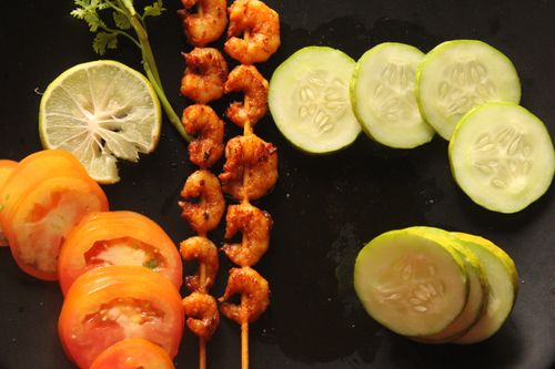Free Appetizing grilled shrimp skewers with fresh cucumber, tomato, and lime slices on a dark background. Stock Photo
