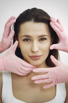 Close-up of a woman receiving a skincare treatment with pink gloves indoors.