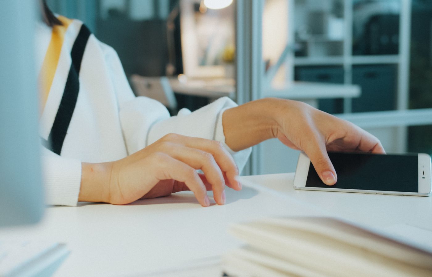 Close-up of a woman's hand using a smartphone at a desk in a modern office setting.