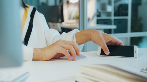 Free Close-up of a woman's hand using a smartphone at a desk in a modern office setting. Stock Photo