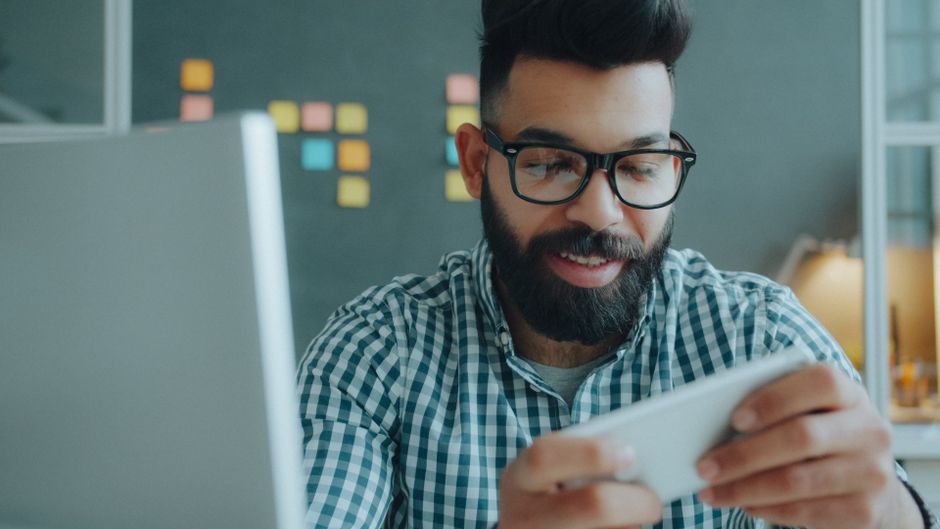 Handsome man with glasses using smartphone at work, enjoying break time.