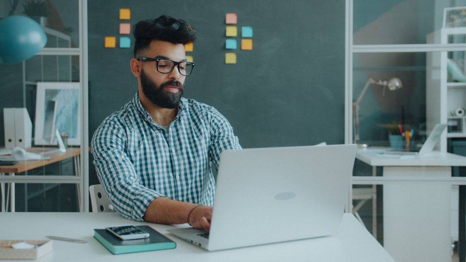 Adult male working on a laptop in a modern office with a creative, organized setting.
