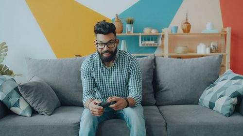Free A man sitting on a comfortable couch while playing video games in a modern living room. Stock Photo